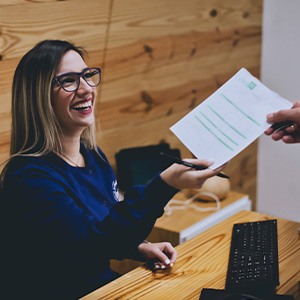 Dental receptionist receives paperwork from patient